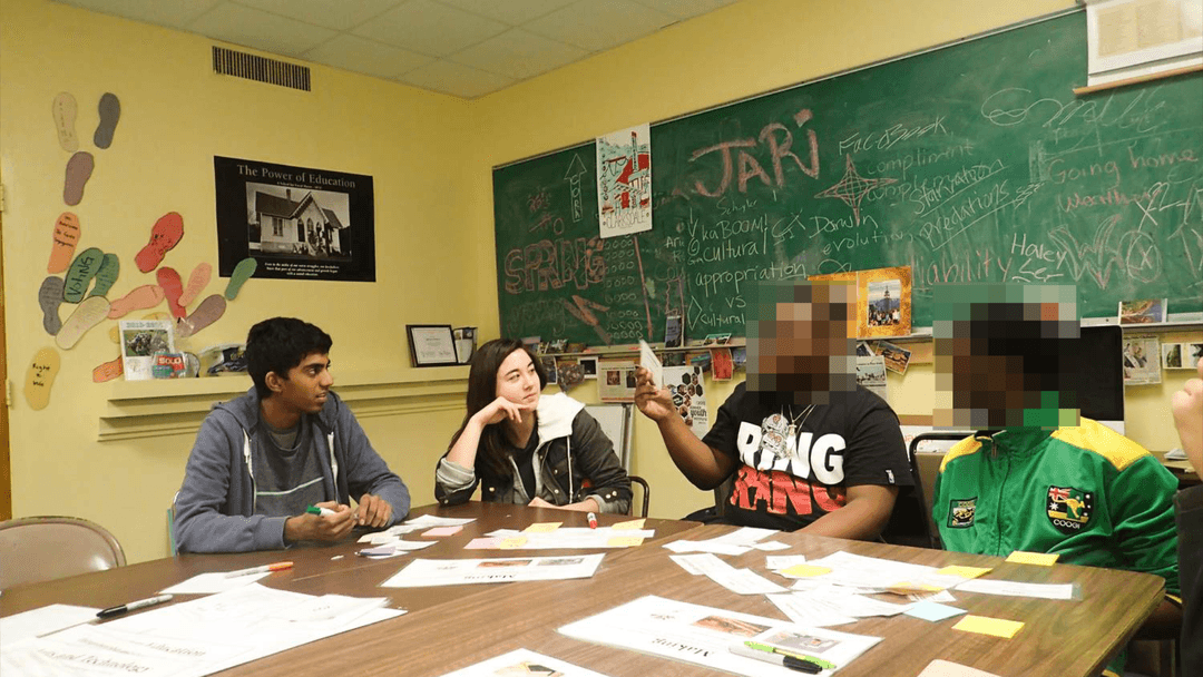 Four people seated around a table in a classroom having a discussion