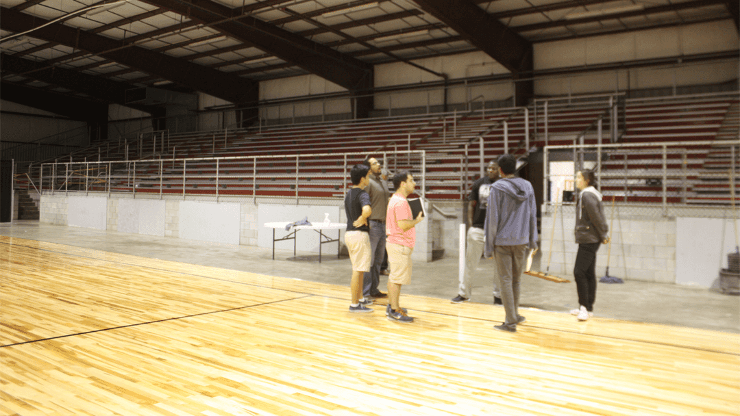 Group of people standing in the middle of a basketball court, having a discussion