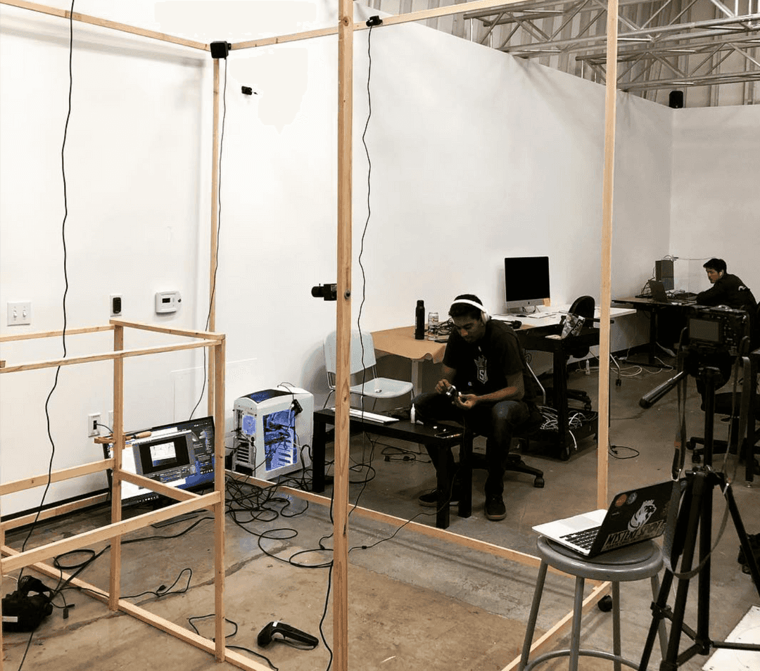 Someone sitting in front of a wooden frame, computer, and tangle of wires.