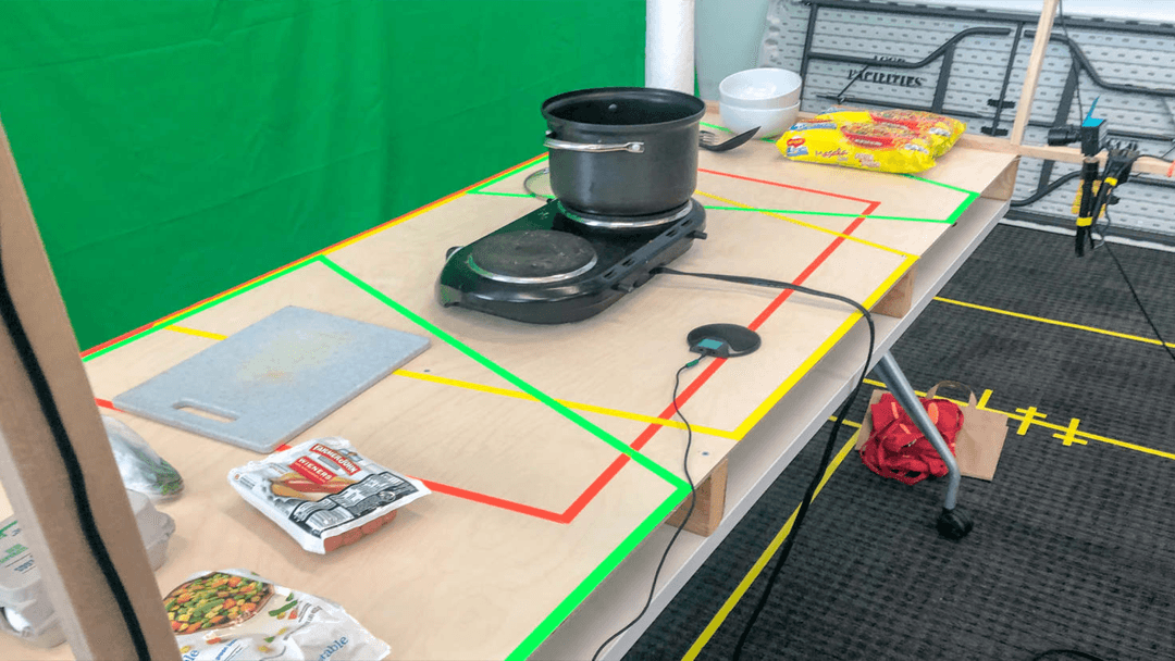A portable burner and groceries on a table covered in colorful taped lines