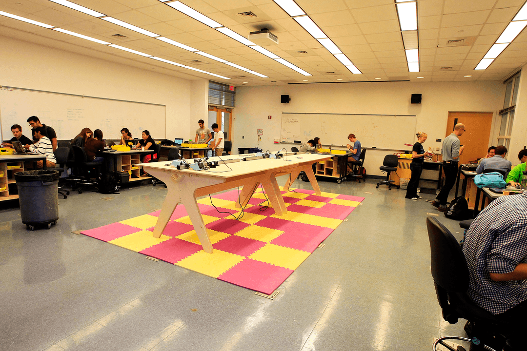 A large wooden center table, surrounded by smaller tables surround by students.